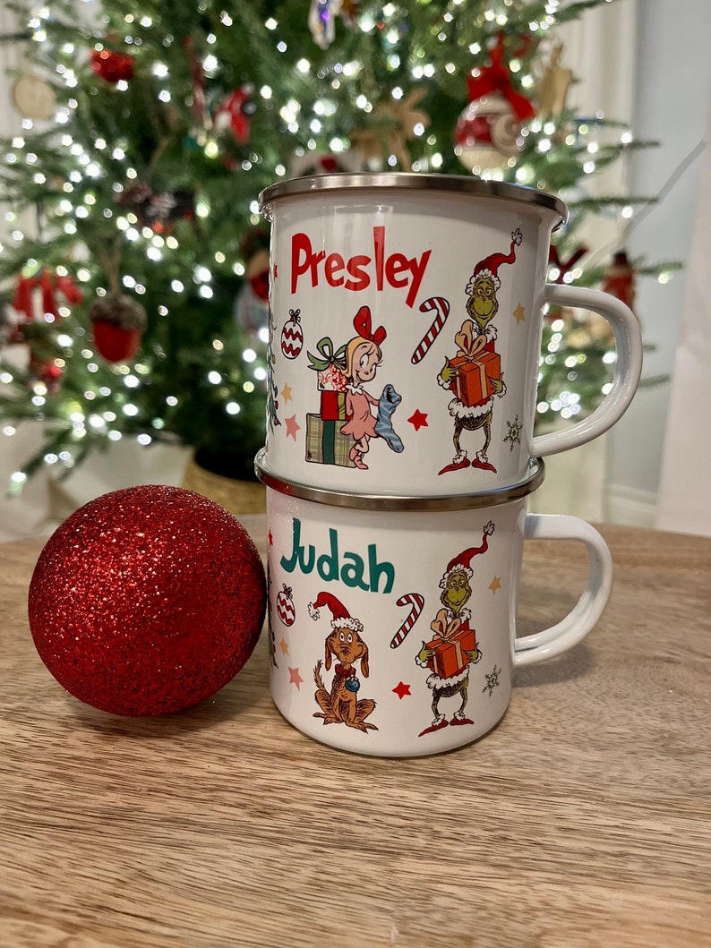 Pu&ograve; includere: Due tazze di smalto bianco con disegni a tema natalizio. La tazza superiore ha il nome "Presley" e la tazza inferiore ha il nome "Judah". Entrambe le tazze presentano un personaggio verde del Grinch, una canna di zucchero rosso e bianca e un ornamento natalizio rosso e bianco.