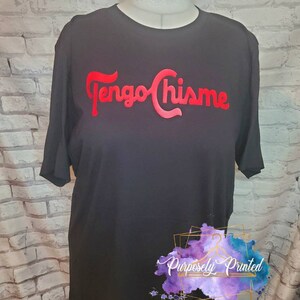 Puede incluir: Camiseta negra con el texto rojo "Tengo Chis-me" impreso en la parte delantera. El texto est&aacute; en una fuente estilizada. La camiseta tiene mangas cortas y cuello redondo. La camiseta est&aacute; en un maniqu&iacute;. El texto "Purposely Printed" es visible en la esquina inferior derecha de la imagen.