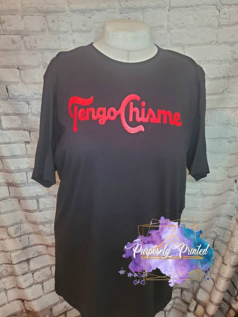 Puede incluir: Camiseta negra con el texto rojo "Tengo Chis-me" impreso en la parte delantera. El texto est&aacute; en una fuente estilizada. La camiseta tiene mangas cortas y cuello redondo. La camiseta est&aacute; en un maniqu&iacute;. El texto "Purposely Printed" es visible en la esquina inferior derecha de la imagen.