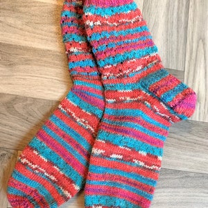 Puede incluir: Un par de calcetines tejidos a mano en un patrón de rayas coloridas de rojo, azul y blanco.