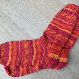 Könnte beinhalten: Ein Paar gestrickte Socken in einem rot-orangen Streifenmuster.