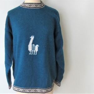 May include: Teal blue knitted sweater with a white llama design. The sweater has a black and white geometric pattern around the neck and hem.
