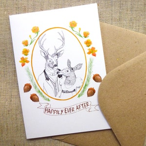 May include: A white card with a drawing of a deer couple in a gold oval frame. The deer are wearing clothes and are kissing. The card has orange flowers and brown acorns around the frame. The text "Happily Ever After" is written on a banner below the frame.