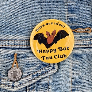 May include: A yellow button with a black bat and the text "Bats are nice! Happy Bat Fan Club".