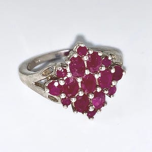 May include: A silver ring with a cluster of oval-cut, deep red gemstones. The gemstones are arranged in a floral or cluster pattern, creating a bold design. The ring has a simple band. The ring is suitable for everyday wear.