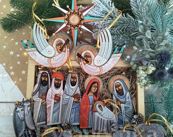 May include: A wooden Christmas ornament set featuring a star, angels, and figures from the Nativity scene. The ornaments are hand-painted with vibrant colors and gold accents. The set includes a wooden box and is decorated with greenery.