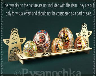 Puede incluir: Un expositor de madera con varios huevos de Pascua decorados. Los huevos presentan patrones y diseños coloridos. Dos recortes de madera de figuras flanquean los huevos. El texto "Pysanochka" está en la parte inferior.