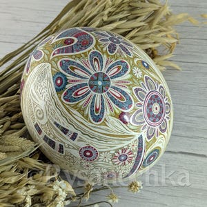 May include: A white egg with a detailed, colorful, floral design. The egg is decorated with intricate patterns in shades of red, blue, green, and gold.