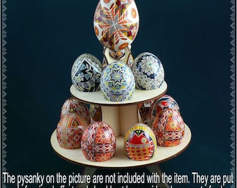 Puede incluir: Un soporte de madera de dos niveles para exhibir huevos de Pascua. El soporte está hecho de madera clara y tiene una base circular. El soporte está decorado con una variedad de huevos pysanky coloridos.
