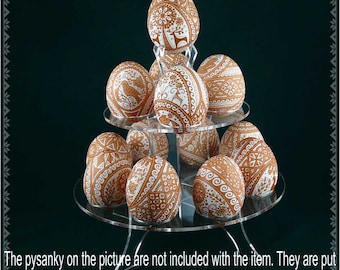 Puede incluir: Un soporte acrílico de tres niveles con 12 huevos pysanky marrones y blancos. Los huevos están decorados con intrincados patrones y diseños geométricos.