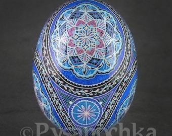 May include: A blue and white intricately decorated Easter egg with a geometric pattern. The egg is painted with a mandala design in shades of blue, white, pink, and black.
