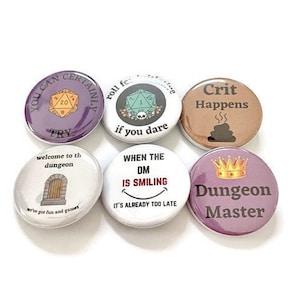 May include: Six round pins with various designs related to Dungeons and Dragons. The pins are white with black text and images. The pins feature a 20-sided die, a skull, a dungeon door, a smiling face, a crown, and a pile of dice.