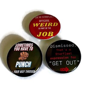 May include: Three round button pins with Star Trek themed sayings. The first pin is red with yellow text that reads "We're Starfleet Officers. Weird is part of the job". The second pin is black with red text that reads "Sometimes you have to punch your way through". The third pin is black with red text that reads "Dismissed. That's a Starfleet expression for "Get Out"".