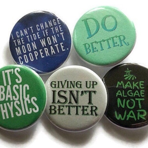 May include: Six round green, blue, white, and black button pins with various sayings. The sayings include "I can't change the tide if the moon won't cooperate", "It's basic physics", "Do better", "Giving up isn't better", "Make algae not war".