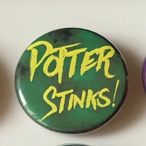 May include: A green button with yellow text that reads "Potter Stinks!" The button is round and has a glossy finish.