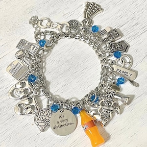 May include: A silver charm bracelet with various charms, including a brain, a bottle of soda, a family charm, and a charm that says "it's a very distinctive..." The bracelet also has blue beads.