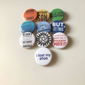 May include: Ten round, colorful button pins with various quotes and designs related to the TV show Supernatural. The quotes include "Saving People, Hunting Things", "Wayward Son", "Get in Loser, We're Going Hunting", "Driver Picks the Music, Shotgun Shuts His  Mouth", "I Think I'm Adorable", "But, Get This", "We Know a Little About a Lot of Things... Just Enough to Make Us Dangerous", "I Hope Your Apple Pie is Freakin' Worth It!" and "I Lost My Shoe".