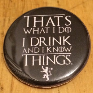 May include: A black button with white text that reads "That's what I do I drink and I know things."  The button also features a white stylized wolf or direwolf.