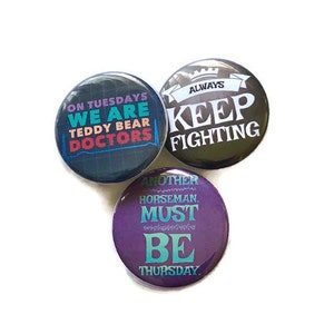 May include: Three round button pins with different sayings. The first pin is black with white text that says "On Tuesdays We Are Teddy Bear Doctors". The second pin is black with white text that says "Always Keep Fighting". The third pin is purple with teal text that says "Another Horseman Must Be Thursday."