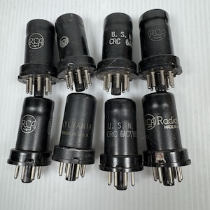 May include: Eight vintage vacuum tubes in black with silver pins. The tubes are marked with brands such as "RCA" and "Sylvania". Some tubes are labeled "U.S. CRC".