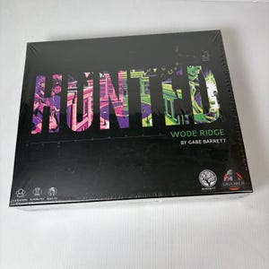 May include: A board game box titled "HUNTED" with "WODE RIDGE" and the author's name, "GABE BARRETT." The box is black with colorful text and graphics. The game is for 1-2 players, takes 50 minutes, and is for ages 13 and up.