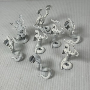 May include: A collection of unpainted miniature fantasy figures. The figures depict snake-like creatures with humanoid upper bodies, some holding weapons or objects. The figures are in various poses, with coiled bodies and upright stances.