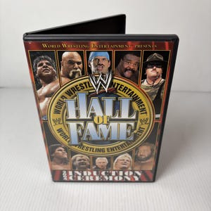 May include: A DVD case for the World Wrestling Entertainment Hall of Fame Induction Ceremony. The cover features images of wrestlers and the text "Hall of Fame" in a gold and blue design. The case is black.