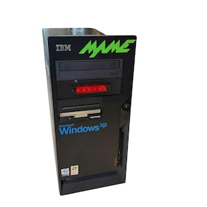 May include: Black IBM computer tower featuring the word "MAME" in green and "Windows XP" in blue. It includes a CD-ROM drive, a floppy disk drive, and a red light. The IBM logo is visible on the top left.