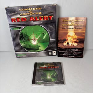 May include: A Command & Conquer: Red Alert PC game set. The box art features a green targeting reticle over a military scene. Includes the game box, a CD-ROM, and a game guide titled "Universe of Games".