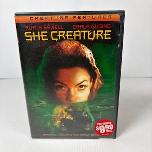 May include: DVD case for the movie "She Creature" featuring Rufus Sewell and Carla Gugino. The cover art shows a woman's face emerging from water, with the title in bold yellow letters. The case has a red sticker that says "Pre-Viewed $9.99".