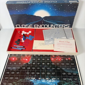 May include: Vintage "Close Encounters of the Third Kind" board game. The box features a night sky scene with a road leading to a bright light. Inside, there are game pieces, cards, and a game board with numbered spaces.