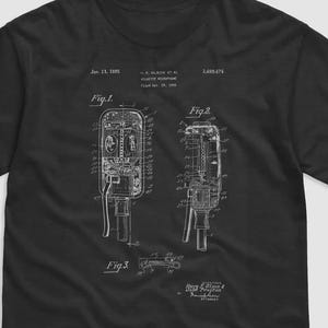 Puede incluir: Camiseta negra con un diagrama esquemático blanco de una máquina, con dibujos técnicos detallados etiquetados como "Fig. 1" y "Fig. 2". La camiseta incluye texto que indica una fecha de patente y el nombre del inventor. Diseño vintage.