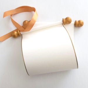 May include: A white scroll with gold trim and gold finials, tied with a light orange ribbon.