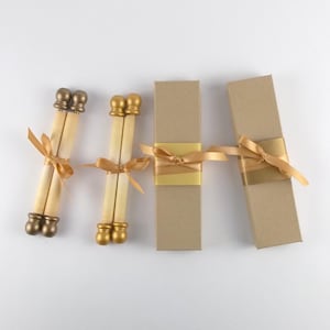 May include: An overhead shot of wedding invitation scrolls and gift boxes. The scrolls are cream-colored with gold-colored finials and tied with gold ribbons. The gift boxes are tan and also tied with gold ribbons.
