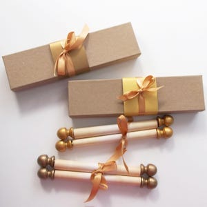 May include: Three white scroll invitations with gold accents and gold ribbon tied around them. The scrolls are in brown boxes with gold ribbon tied around them.