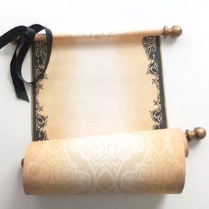 May include: A rolled up scroll with a black ribbon and gold accents. The scroll has a decorative border with a floral pattern. The scroll is made of parchment paper and is blank.