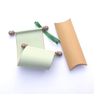 May include: A light green scroll with bronze-colored finials and a matching gift box. The scroll is partially unrolled, revealing the paper inside. Green ribbon is tied to the scroll. The gift box is a light brown color.
