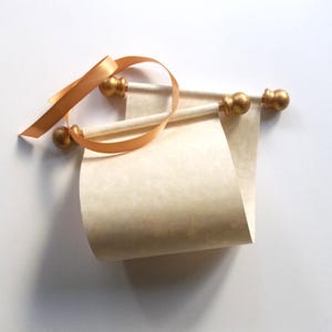 May include: A blank scroll with gold-colored wooden dowels and a gold satin ribbon. The scroll is rolled up and tied with the ribbon.