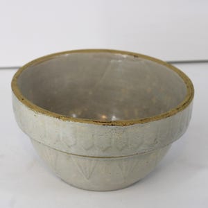 Peut inclure: Un bol mélangeur en céramique ronde avec un vernis gris clair et un bord beige. L'extérieur présente un motif répétitif en relief de pétales ou d'éventails sur les sections supérieure et inférieure. L'intérieur est lisse et gris clair.