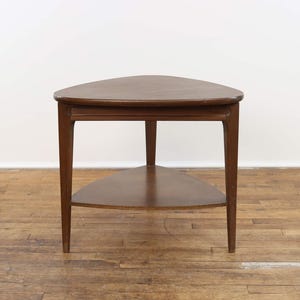 May include: A triangular wooden end table with a lower shelf. The table has a dark brown finish and a simple design.