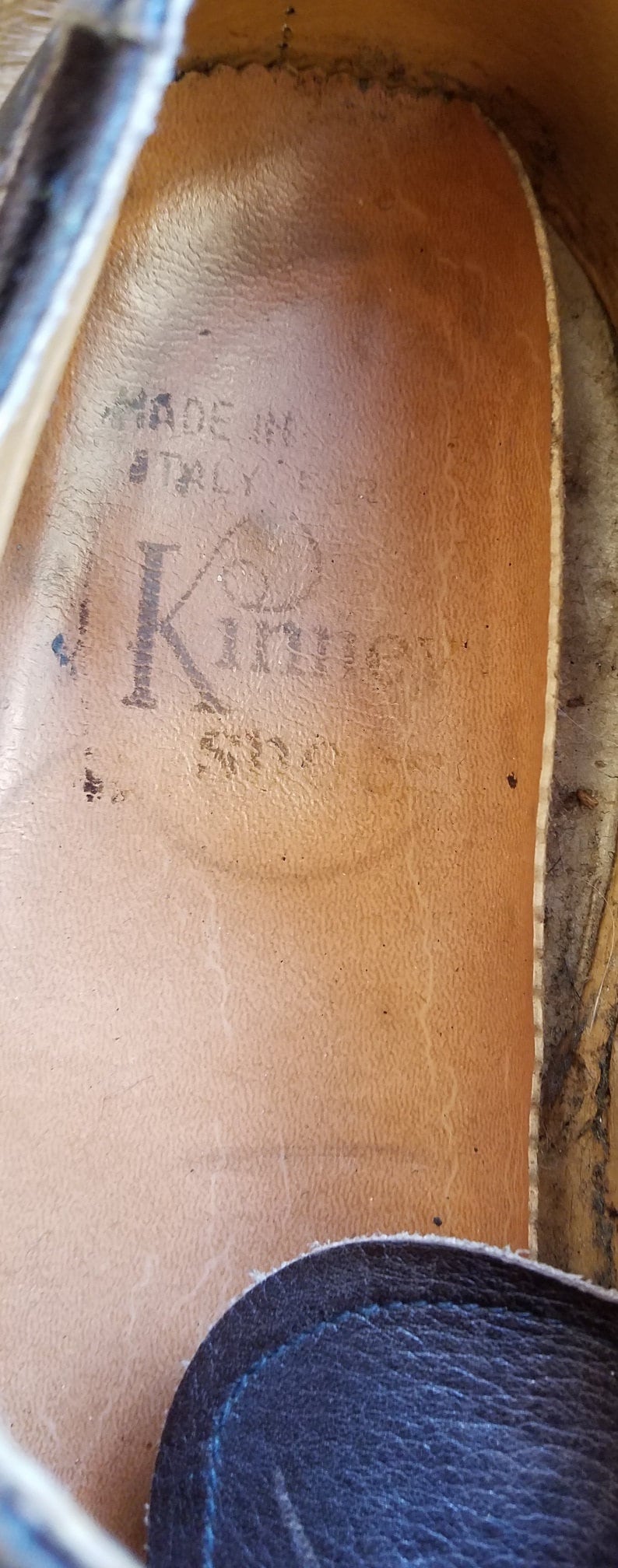 May include: Close-up of the inside of a brown leather shoe with the text "Made in Italy" and "K" with a circle around it.