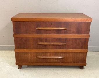 May include: A three-drawer dresser made of wood with a light brown finish. The dresser has three drawers with wooden pulls. The dresser is sitting on a light gray floor.