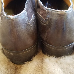 May include: A pair of brown leather shoes with laces. The shoes have a brogue design and are sitting on a light brown fur surface.