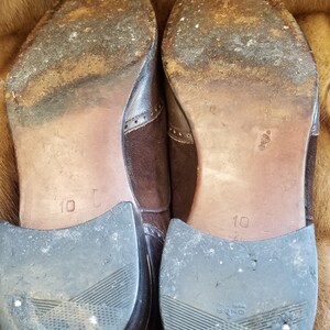 May include: A pair of brown leather shoes with suede accents. The shoes have a black rubber sole and are size 10.