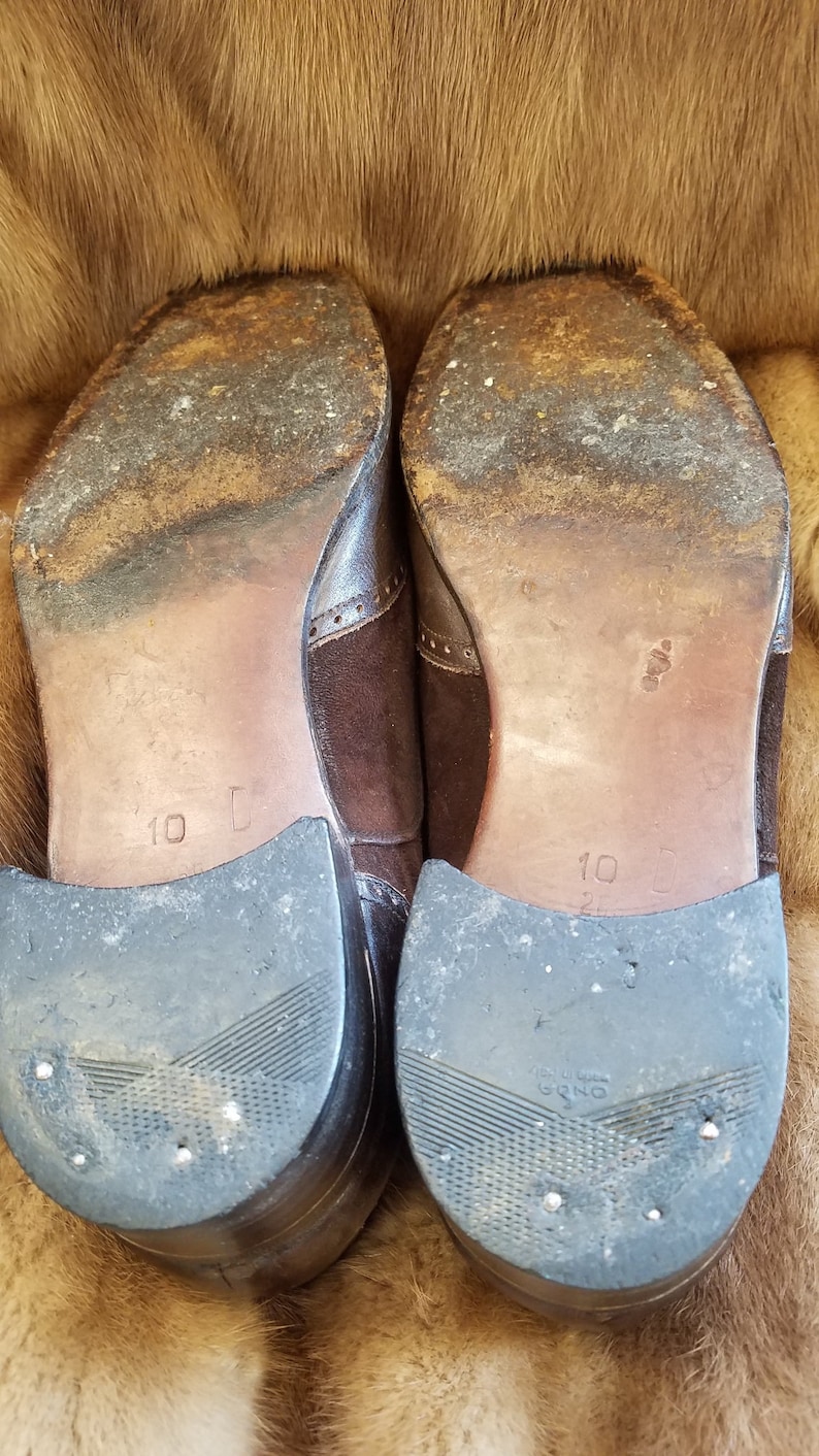 May include: A pair of brown leather shoes with suede accents. The shoes have a black rubber sole and are size 10.