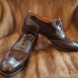 May include: A pair of brown leather and suede lace-up shoes with wingtip detailing. The shoes are on a faux fur background.