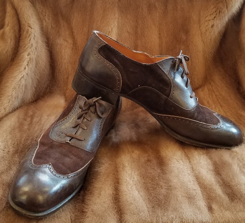 May include: A pair of brown leather and suede lace-up shoes with wingtip detailing. The shoes are on a faux fur background.