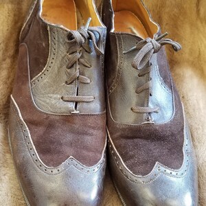 May include: A pair of brown leather and suede wingtip shoes with laces. The shoes have a brogue design and a polished finish.