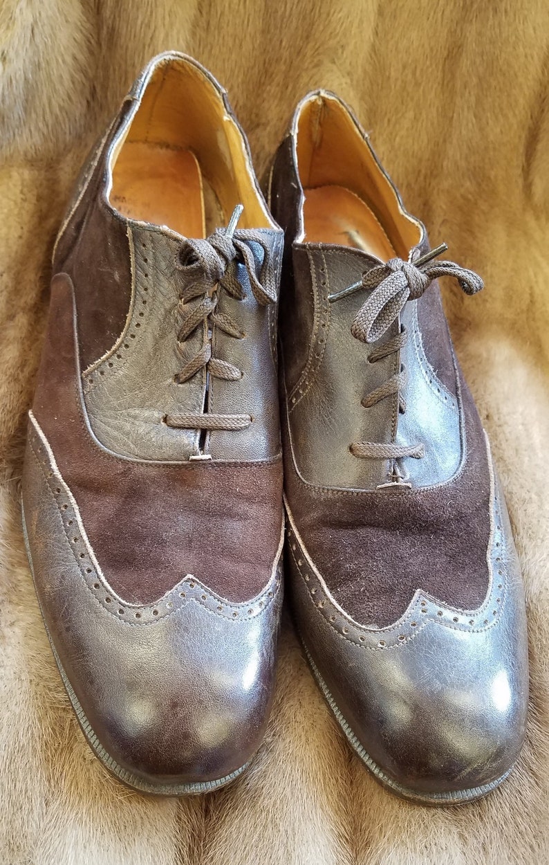 May include: A pair of brown leather and suede wingtip shoes with laces. The shoes have a brogue design and a polished finish.
