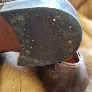 May include: Close-up of the bottom of a brown leather shoe with a black rubber sole. The sole has a textured pattern and the words "Oxford Made in India" are visible.